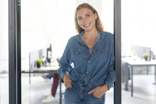 Cheerful businesswoman standing in office environment. Young female executive standing and looking at camera - Valokuva, kuva