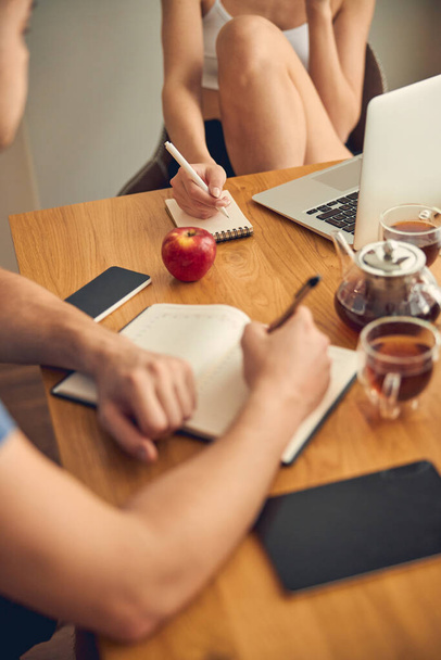Duas pessoas escrevendo notas perto de laptop na mesa marrom - Foto, Imagem