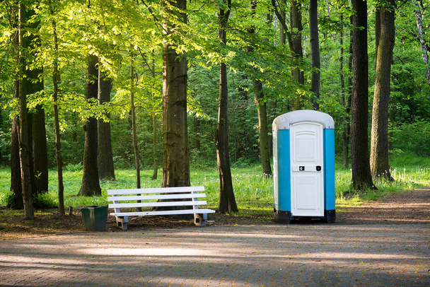 WC portátil en un parque de primavera, al lado del camino y el banco blanco. - Foto, imagen
