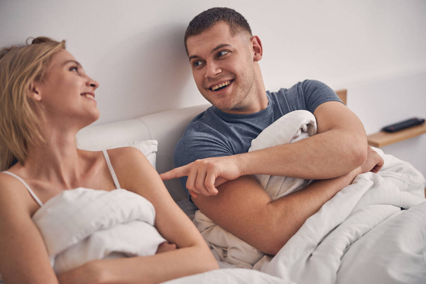 Beautiful married couple lies in bedroom laughing - Фото, изображение