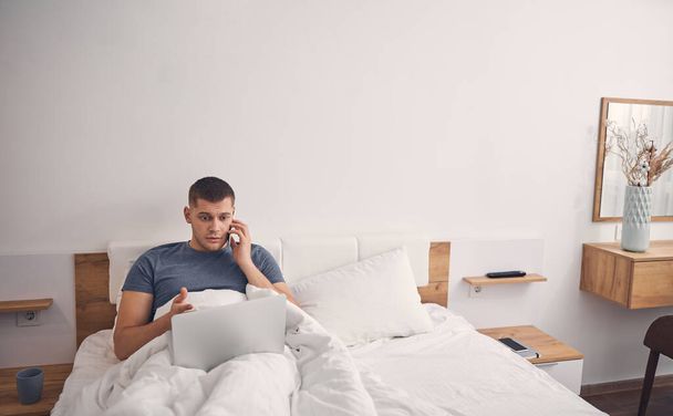 Úzkostlivý muž pracující online z domova v ložnici - Fotografie, Obrázek
