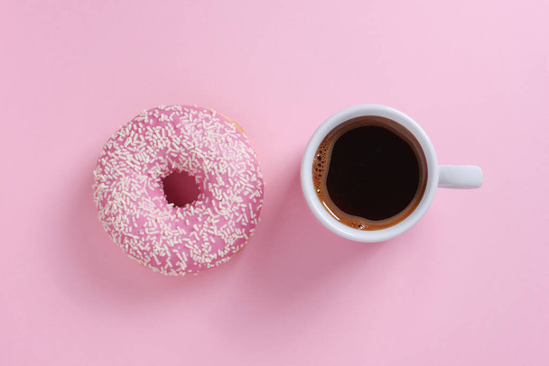 ピンクの背景にコーヒーのスプリンクルとカップでドーナツ、トップビュー - 写真・画像