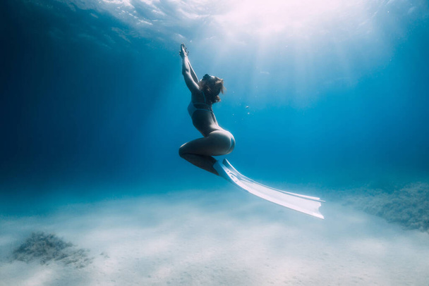 Atrakcyjna kobieta freediver ślizga się i pozuje nad piaszczystym dnem z białymi płetwami. - Zdjęcie, obraz