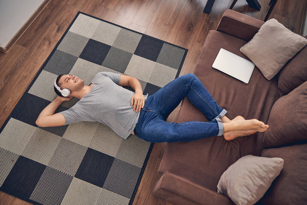 Привлекательный брюнетка мужчина расслабляется на ковре, слушая музыку - Фото, изображение