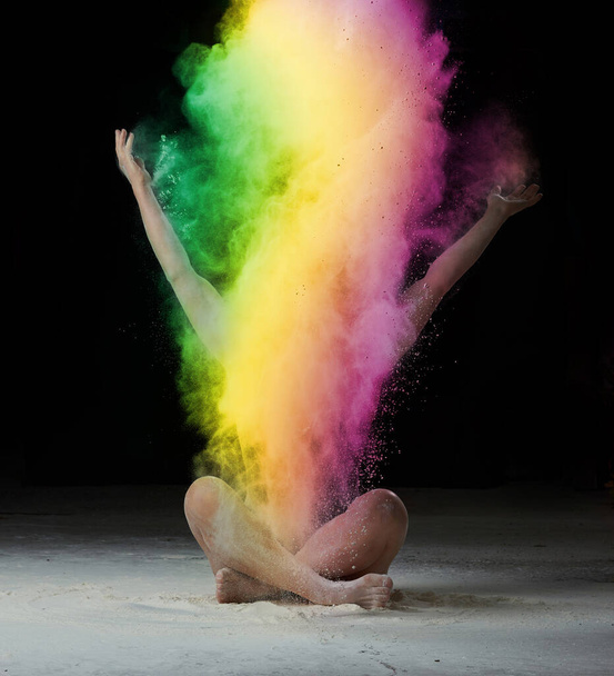 caucasian woman sits on the floor and throws colored powder up, black background - Foto, Imagem