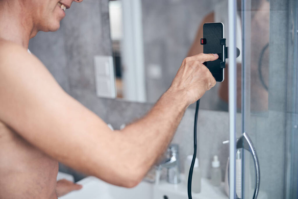 Tevreden man met zijn smartphone in een badkamer - Foto, afbeelding