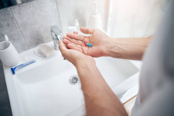 Kaukasische Männerhände mit Vitaminen im Badezimmer - Foto, Bild