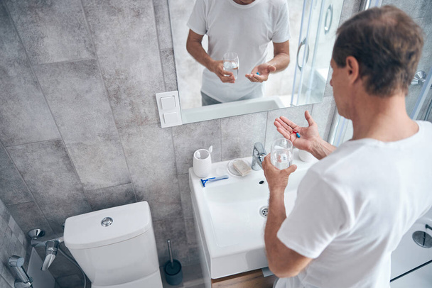Hombre con suplementos dietéticos de pie ante el espejo - Foto, imagen