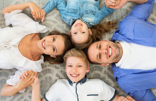 Perhe makaa kädet hymyilevä posing lattialla sisätiloissa, edellä View - Valokuva, kuva