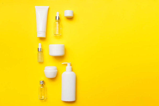 Kozmetikai palackok élénk sárga háttérrel, felülnézetben, másolás. Gúnyolódj! Fehér üvegek, fürdőkellékek. Arc és testápolás fogalma. - Fotó, kép