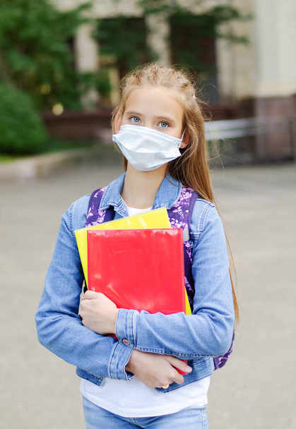 Little girl child with face mask and backpack. Education concept. Back to school after covid-19.  Preteen student holding the books outdoors. - Photo, image