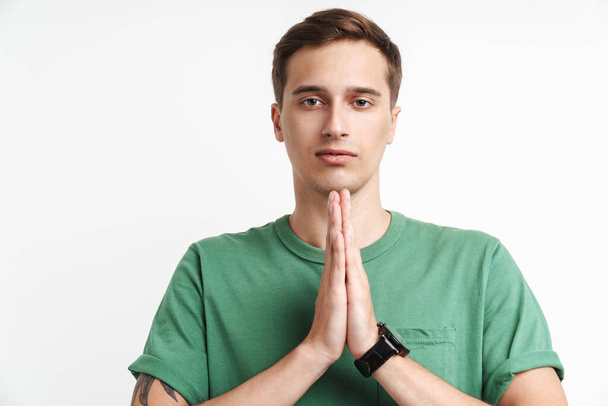 Image of focused caucasian man in basic t-shirt praying and holding palms together isolated over white background - Фото, зображення