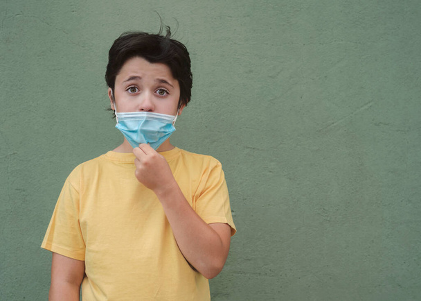 kid who lowers the medical mask over green background - Photo, Image