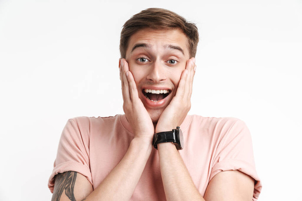 Image of excited caucasian man in basic t-shirt smiling and grabbing his face isolated over white background - Fotografie, Obrázek