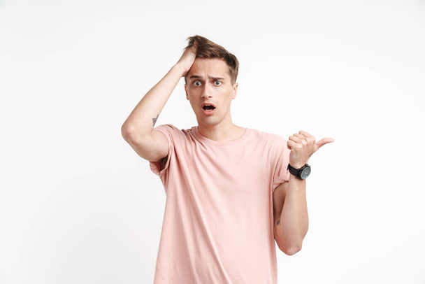 Image of shocked caucasian man in basic t-shirt screaming and pointing finger aside isolated over white background - Foto, immagini
