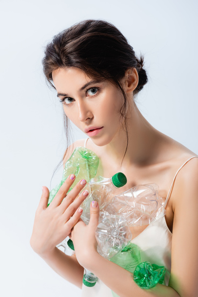Esmer kadın elinde plastik şişelerle beyaz ekoloji konseptine izole edilmiş kameraya bakıyor.  - Fotoğraf, Görsel