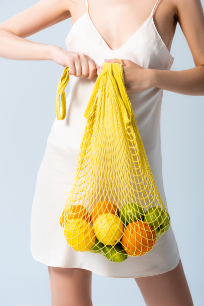 vista recortada de la mujer en vestido de seda sosteniendo bolsa de hilo con frutas en blanco, concepto de ecología  - Foto, Imagen