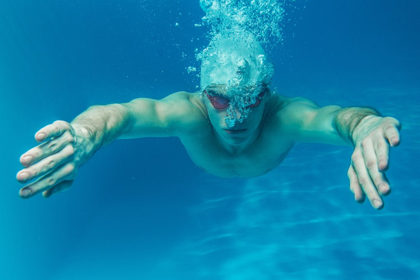 άνθρωπος στο σκουφάκι και googles κάτω από το νερό στην πισίνα - Φωτογραφία, εικόνα
