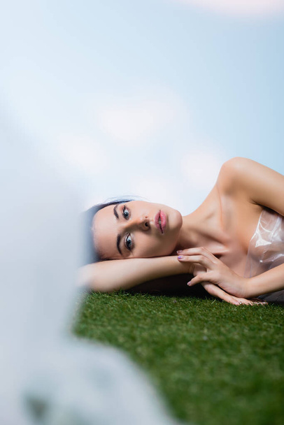 selective focus of young model lying near polyethylene on grass, ecology concept  - Photo, Image