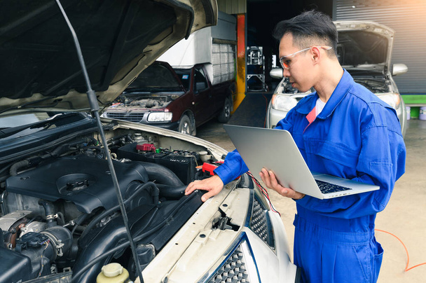 Technik azjatycki analizuje wykres silnika samochodu na laptopie w garażu. koncepcja motoryzacji, naprawy, mechaniki, pojazdów i technologii. - Zdjęcie, obraz