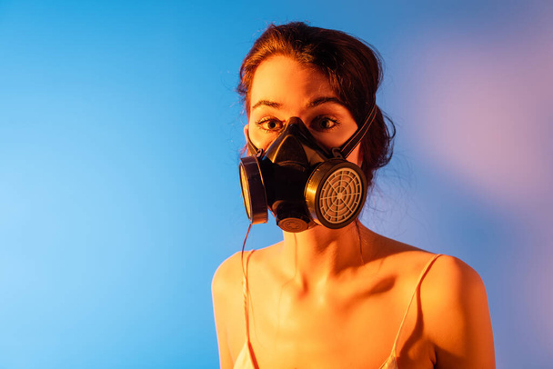 brunette model in gas mask looking at camera on blue - Foto, afbeelding