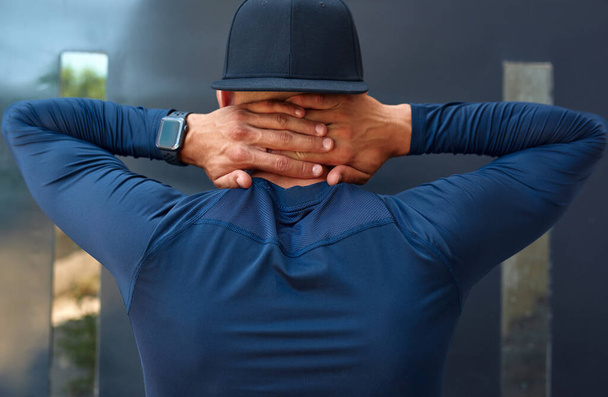 Rear view of healthy athlete man in blue sportswear with his arms on the neck before exercising outdoors. Fitness urban male  getting ready before running in the city street. - Фото, изображение