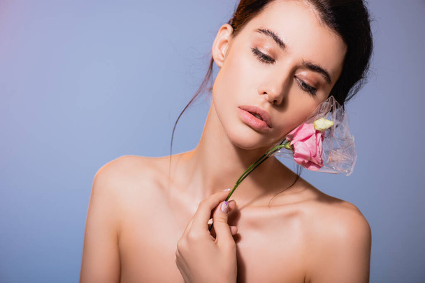 young and naked woman holding flowers in polyethylene isolated on grey, ecology concept  - Photo, image