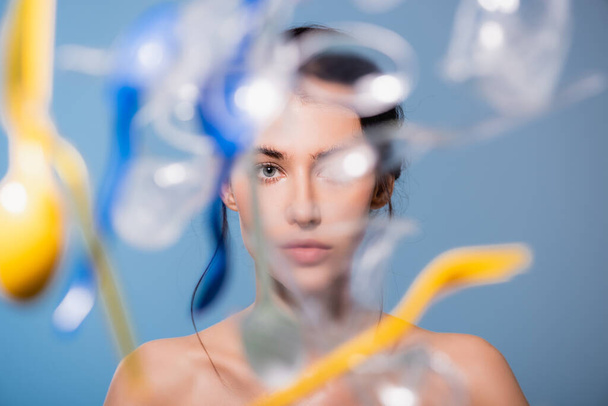 selective focus of naked woman near falling plastic cups, spoons and forks on blue, ecology concept  - Foto, Bild
