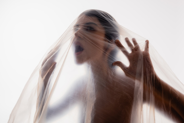 mujer morena atrapada gritando a través de polietileno aislado en blanco, concepto de ecología - Foto, Imagen