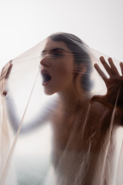 mujer joven gritando a través de polietileno aislado en blanco, concepto de ecología - Foto, Imagen