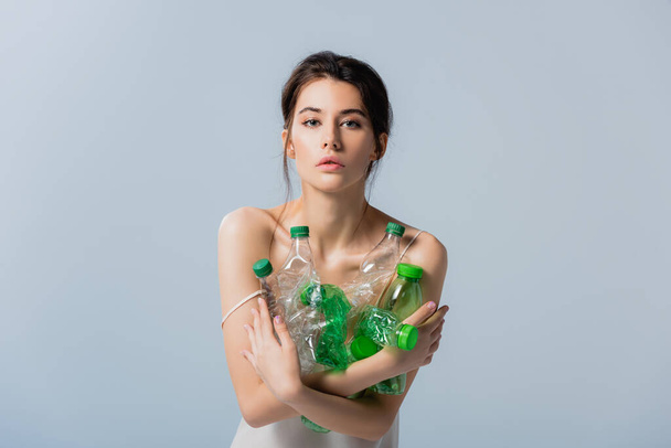 brunette woman looking at camera and holding plastic bottles isolated on grey, ecology concept  - Foto, immagini