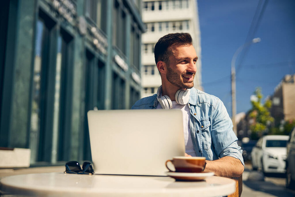 Θετική ευχαριστημένος ελεύθερος επαγγελματίας κάθεται μπροστά από το laptop του - Φωτογραφία, εικόνα