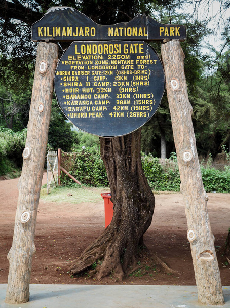 вывеска базового лагеря. проводники и шерпы нести тяжелые мешки, как они поднимаются на гору Килиманджаро - Фото, изображение