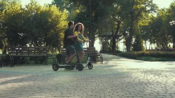 Jong stel paardrijden elektrische scooter in het park met ochtendzon fakkels - Video
