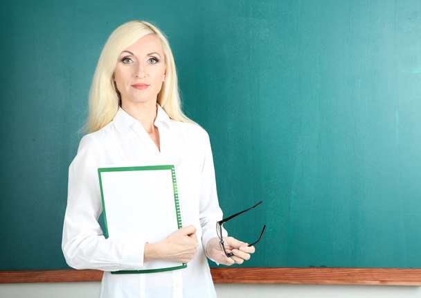 δάσκαλος σε σχολείο κοντά μαυροπίνακα με φάκελο στην τάξη - Φωτογραφία, εικόνα