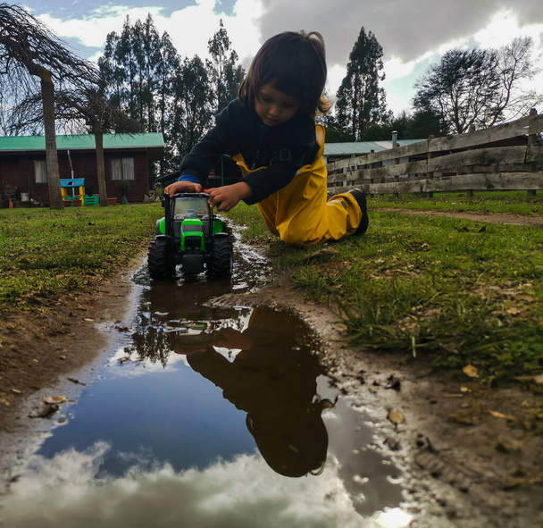 泥の水たまりの中でおもちゃのトラクターで遊ぶ子供 - 写真・画像