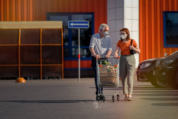                    Senior couple with face masks and shopping walking outside supermarket                 - Foto, Imagem