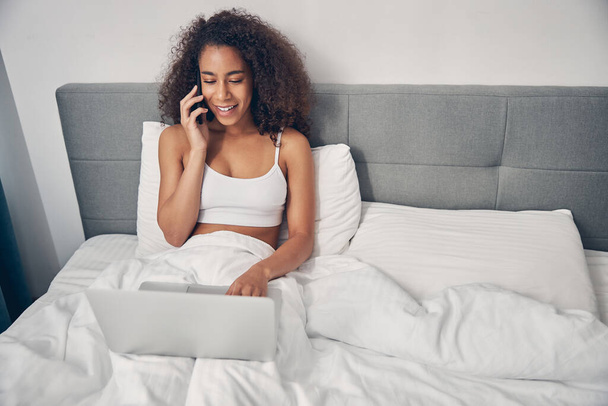 Женщина с телефоном сидит в постели - Фото, изображение