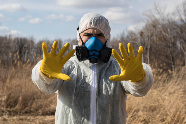 Muž v chemickém ochranném obleku a respirátor pod širým nebem ukazuje stopku oběma rukama. Znečištění ovzduší. Koncepce čínského pandemického koronaviru. - Fotografie, Obrázek