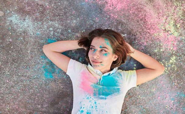 Glad woman resting on ground during paint party - Foto, Imagen