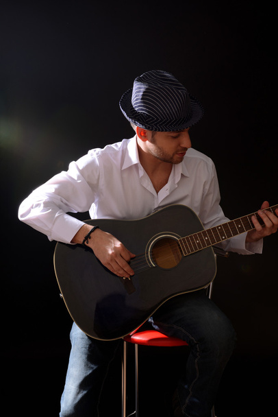 Young musician playing acoustic guitar and singing, on dark background - Foto, imagen