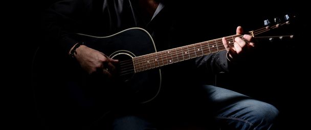 Young musician playing acoustic guitar and singing, on dark background - Foto, afbeelding