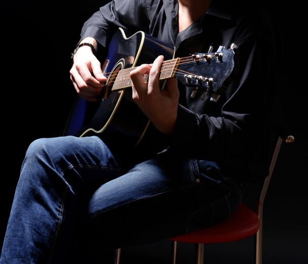 Young musician playing acoustic guitar and singing, on dark background - Fotó, kép