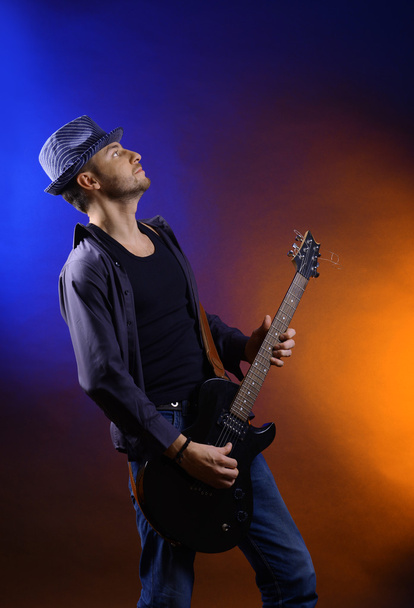 Young musician playing guitar on dark color background - Фото, изображение