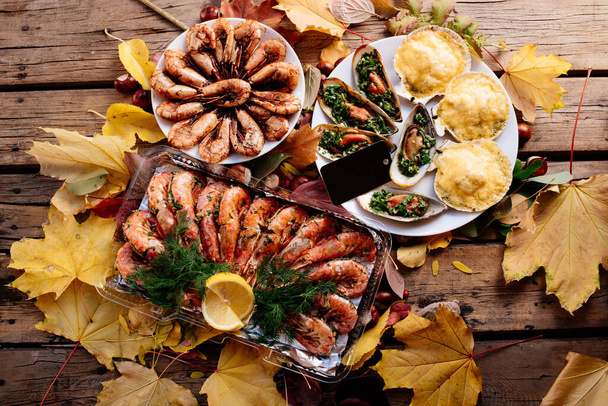 Fried shrimps, baked mussels and scallops baked under cheese on wooden table with autumn leaves and chestnuts. for Oktoberfest - Fotografie, Obrázek