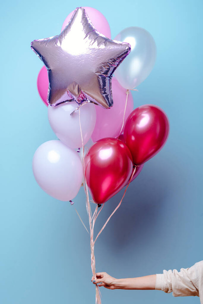 Composition of red, pink, transparent helium balloons and silver star in the hand of a woman on a blue background. - Foto, Bild