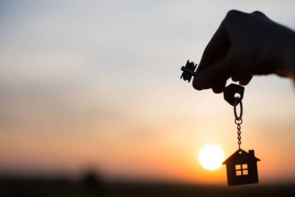 Silhouette of a house figure with a key, a pen with a keychain on the background of the sunset. They dream of a house, building, moving to a new house, mortgages, renting and buying real estate. Copy space - Fotoğraf, Görsel