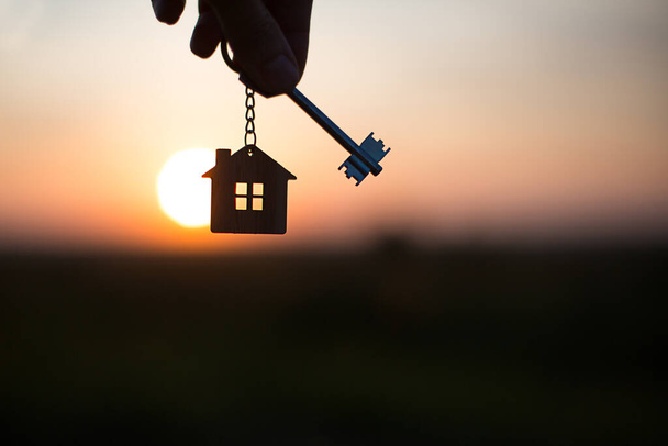 Silhouette of a house figure with a key, a pen with a keychain on the background of the sunset. They dream of a house, building, moving to a new house, mortgages, renting and buying real estate. Copy space - Photo, Image