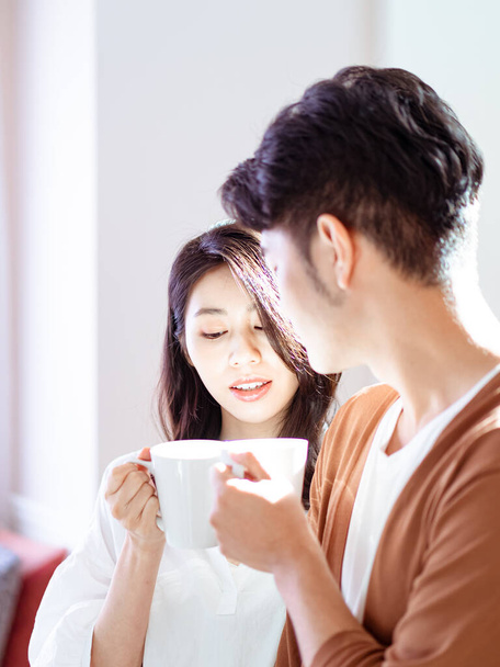 Joven asiático mujer y hombre están disfrutando de pasar tiempo juntos en casa con taza de café en las manos. - Foto, imagen