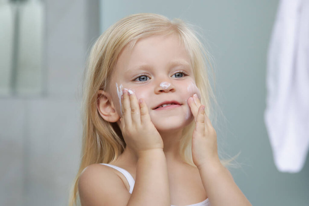 Чарівна блондинка кавказька дівчинка наносить крем на її обличчя
 - Фото, зображення